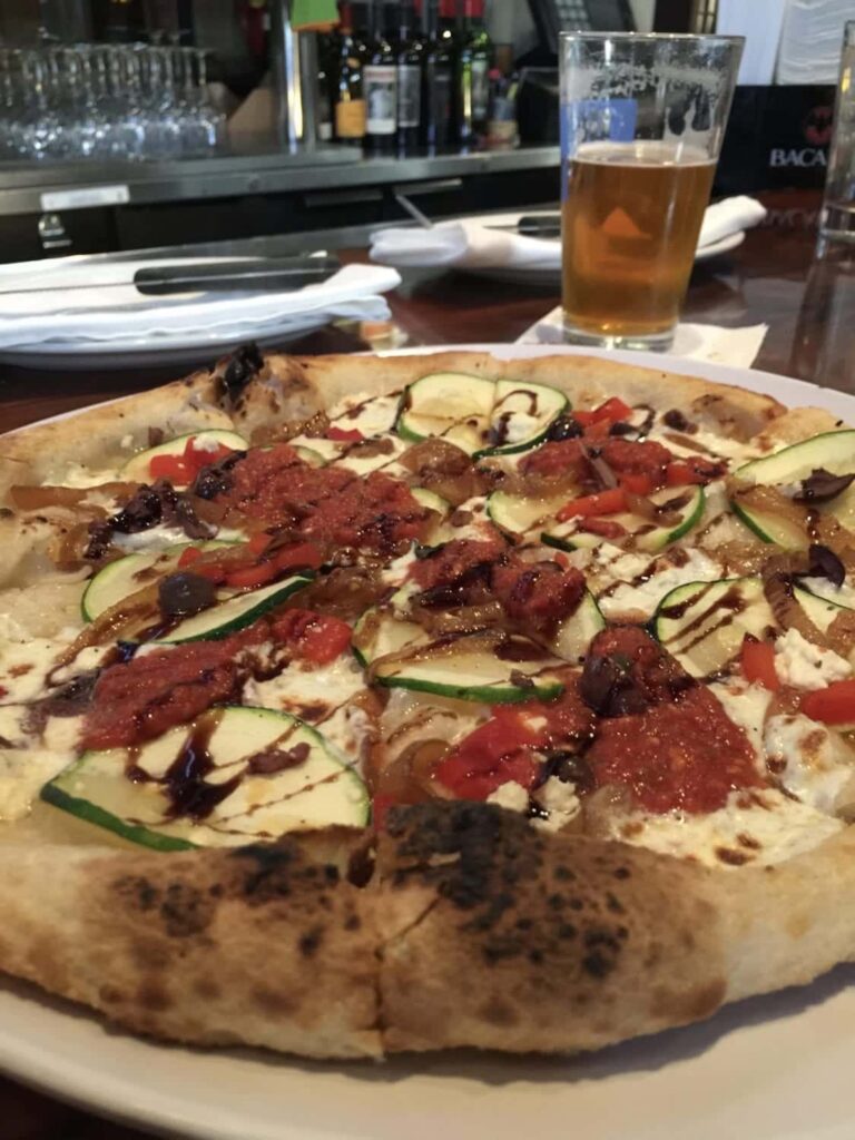 A pizza on a plate with a glass of beer in the background.