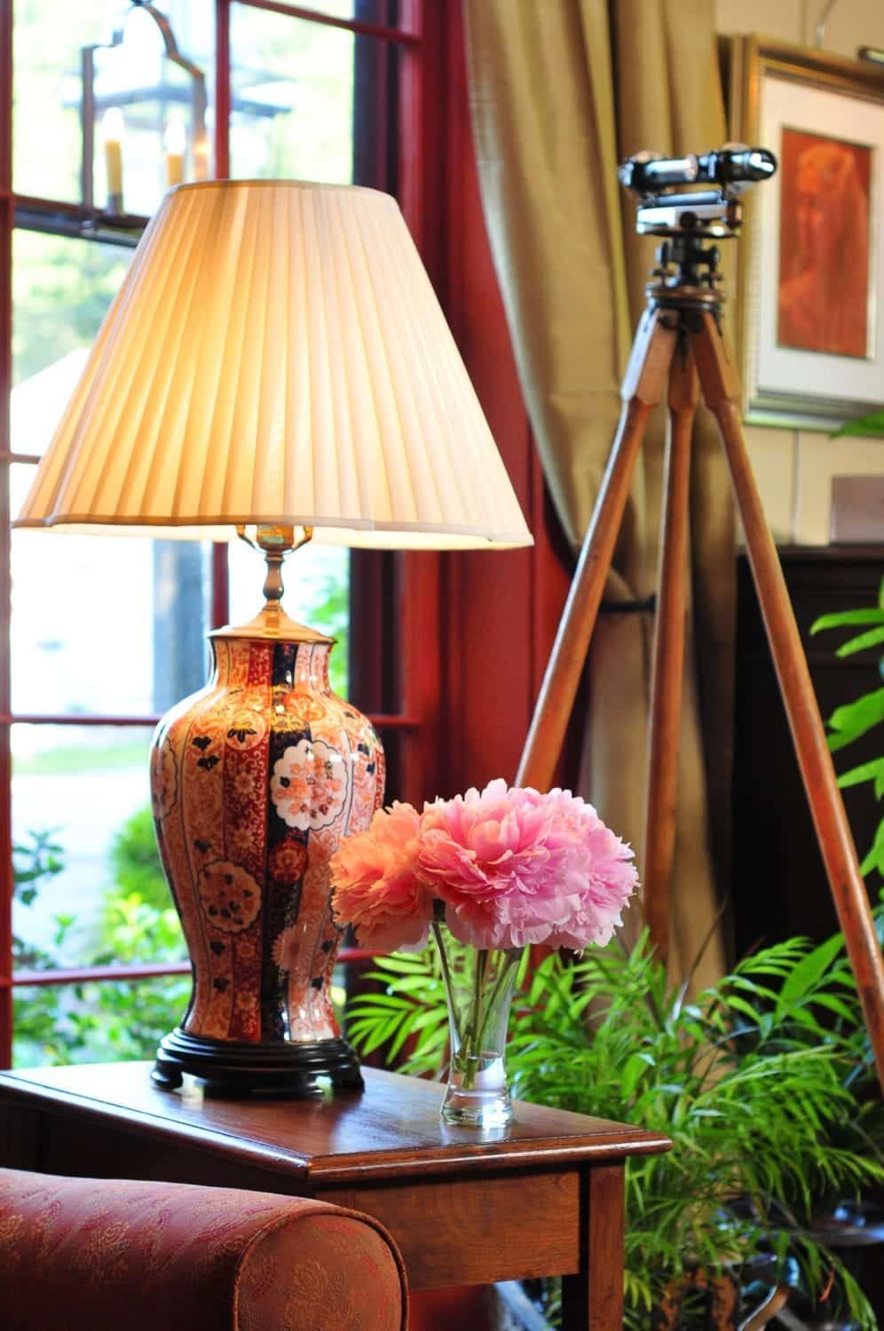 A lamp sits on a table next to a vase of pink flowers.