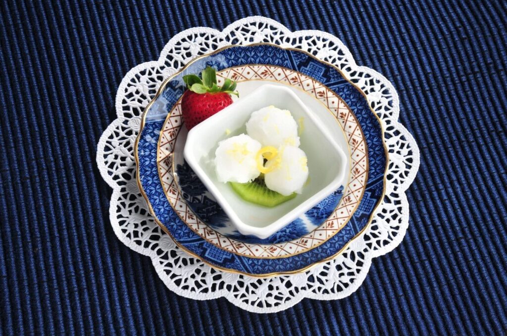 A blue and white plate with a bowl of fruit and a strawberry on it.