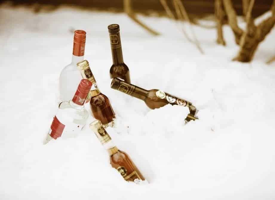 Three bottles of alcohol are laying in the snow.