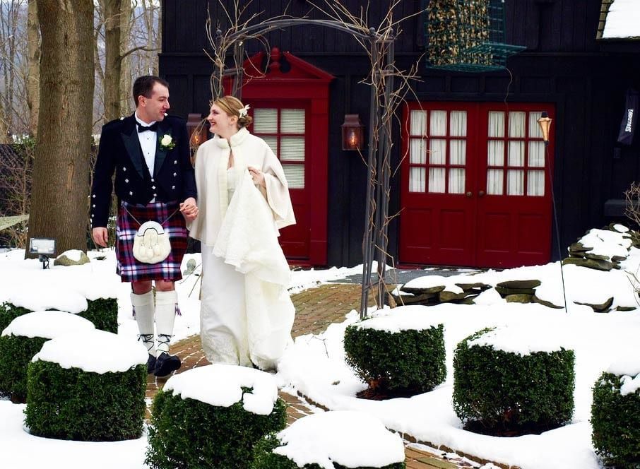 A bride and groom are walking in the snow in front of a red garage door.
