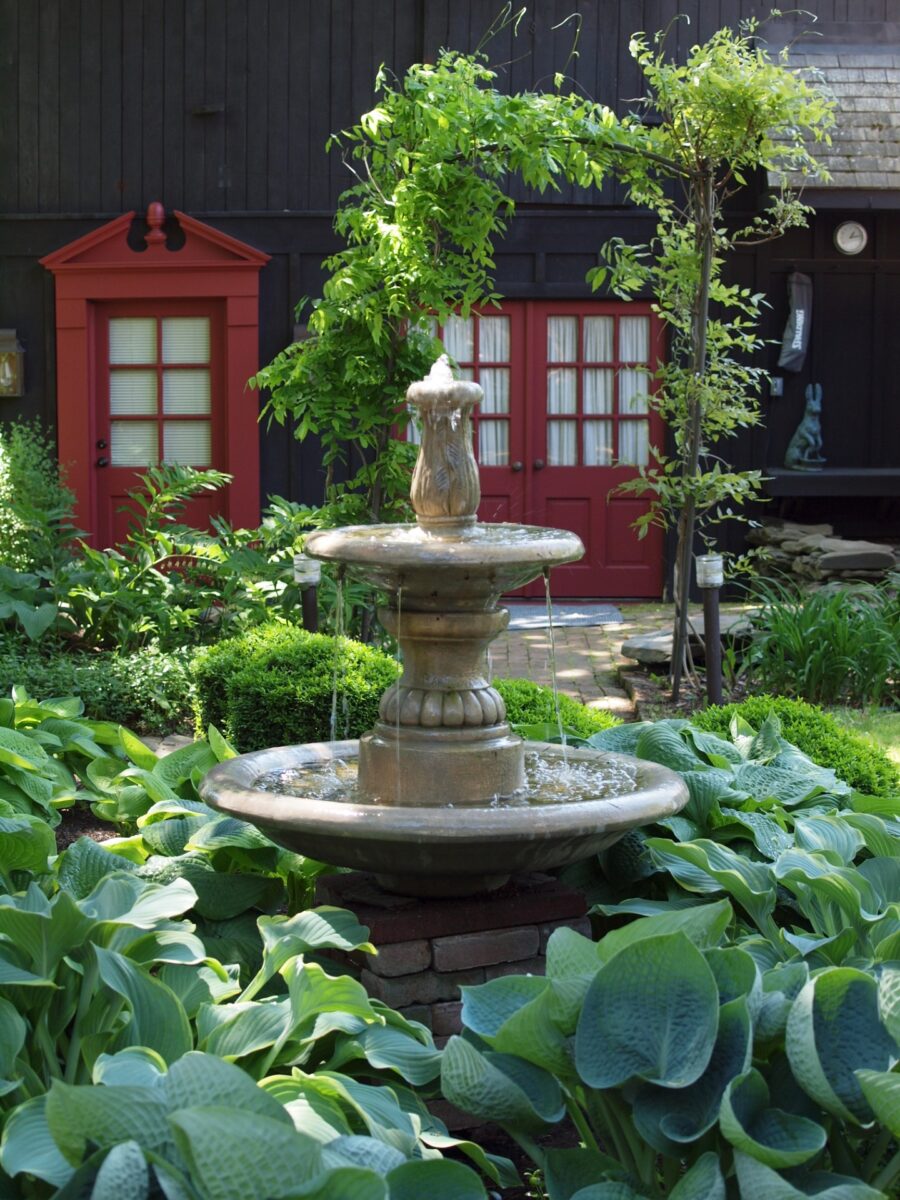A fountain in a garden in front of a red phone booth.